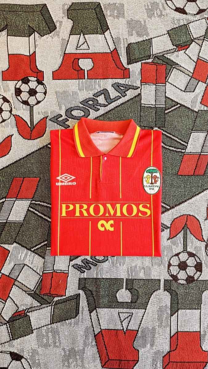 A vintage red Umbro soccer jersey with yellow stripes and 'PROMOS' sponsor text, laid flat on a patterned textile background featuring football motifs.